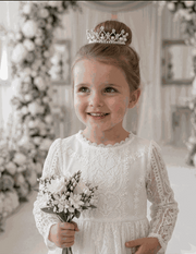 Toddler girl wearing a long white lace fairy dress with vintage floral details and puff sleeves.